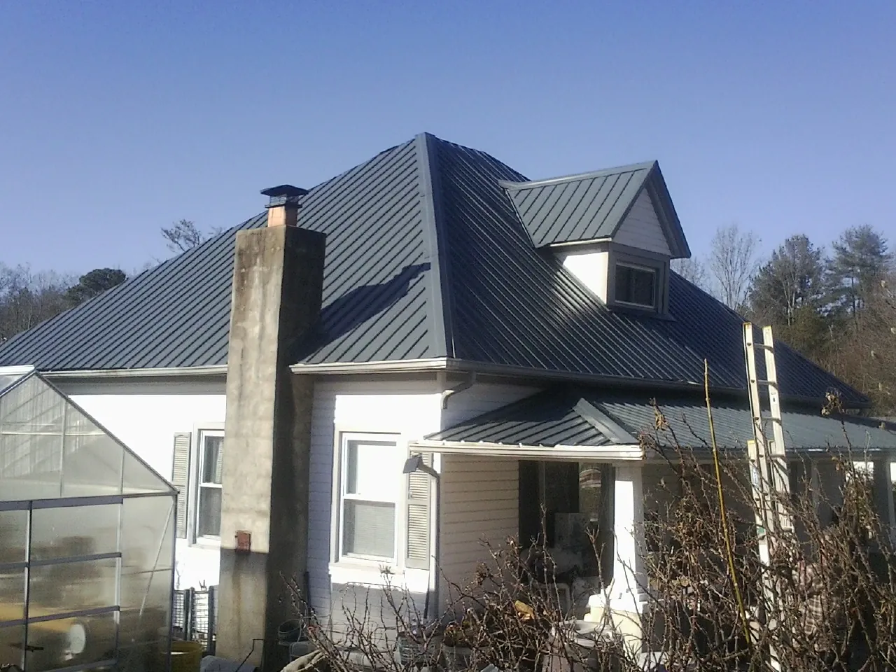 Dark blue standing seam metal roof on a white farmhouse with dormer — Slate & Tile Roof Repair by Roofing Brothers in Weems