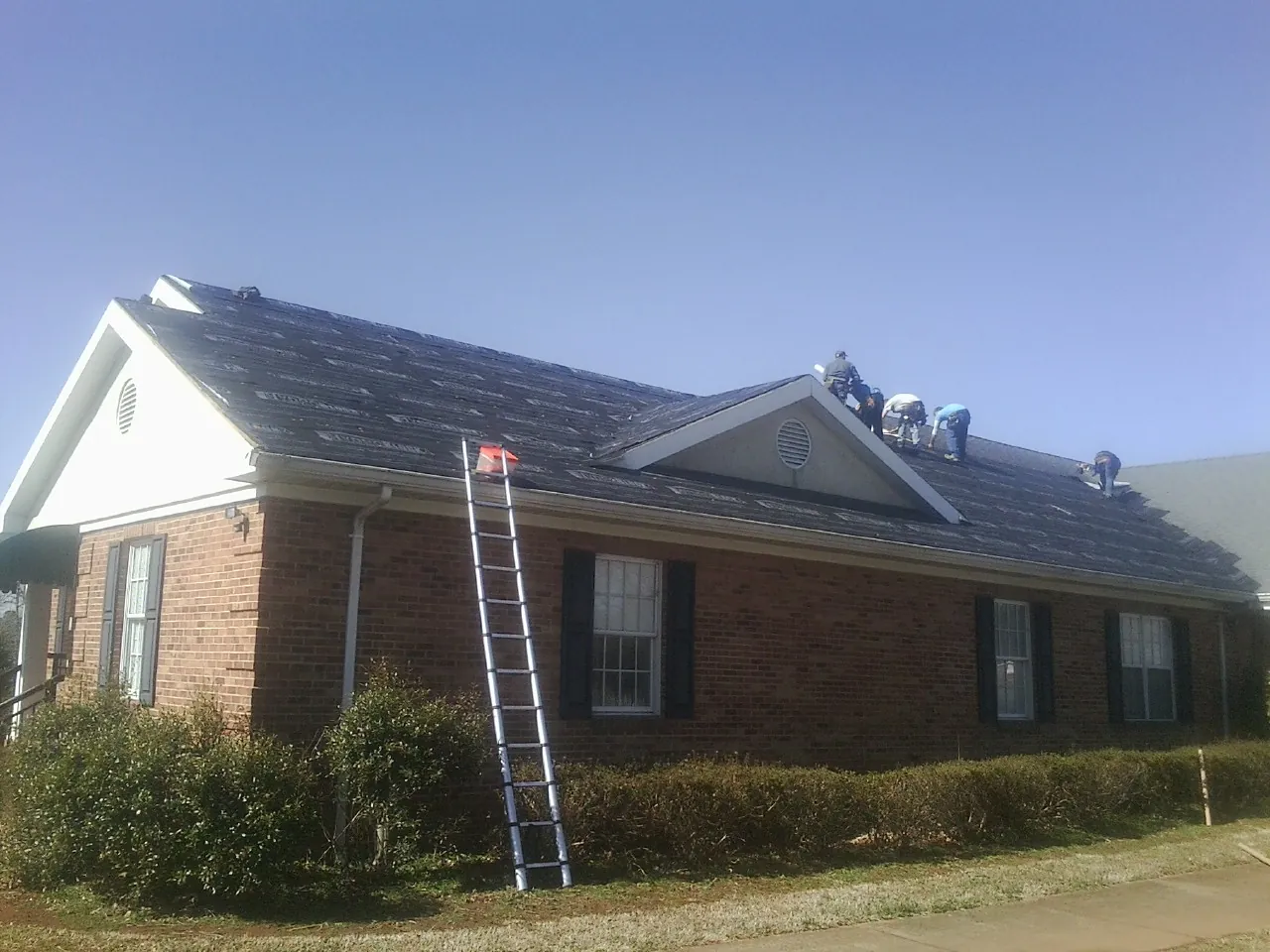 Crew tearing shingles off a brick ranch roof with a ladder set — Emergency Roof Repair work by our crew in Weems