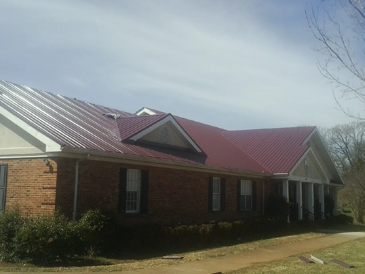 Red metal roof with gabled entries on a long brick building, from a Hail Damage Roof Repair job in Weems