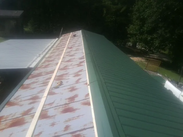 Old rusted panels beside newly installed green metal roofing — Wind Damage Roof Repair by Roofing Brothers in Weems