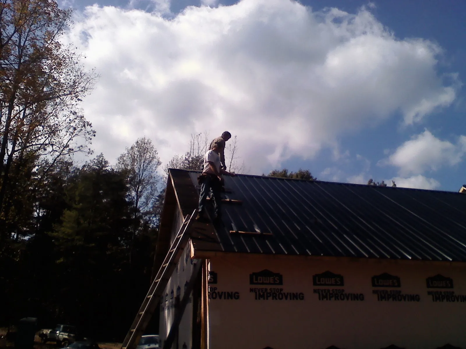 Roofer fastening dark metal panels high against a cloudy sky, from a Roof Inspection job in Weems