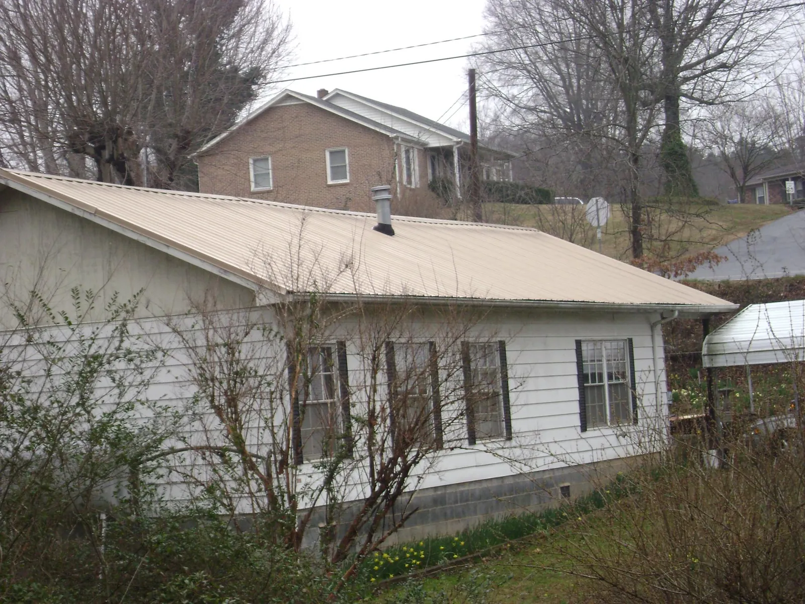 Tan metal roof on a white sided house set into a hillside — Commercial Roofing by Roofing Brothers in Weems
