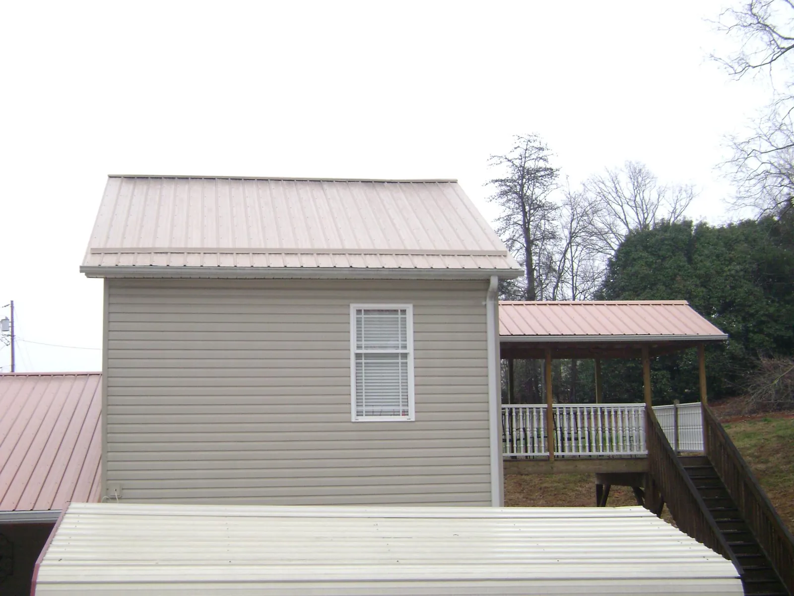 Tan metal roofs on a two story addition and attached porch, from a Roof Replacement job in Weems